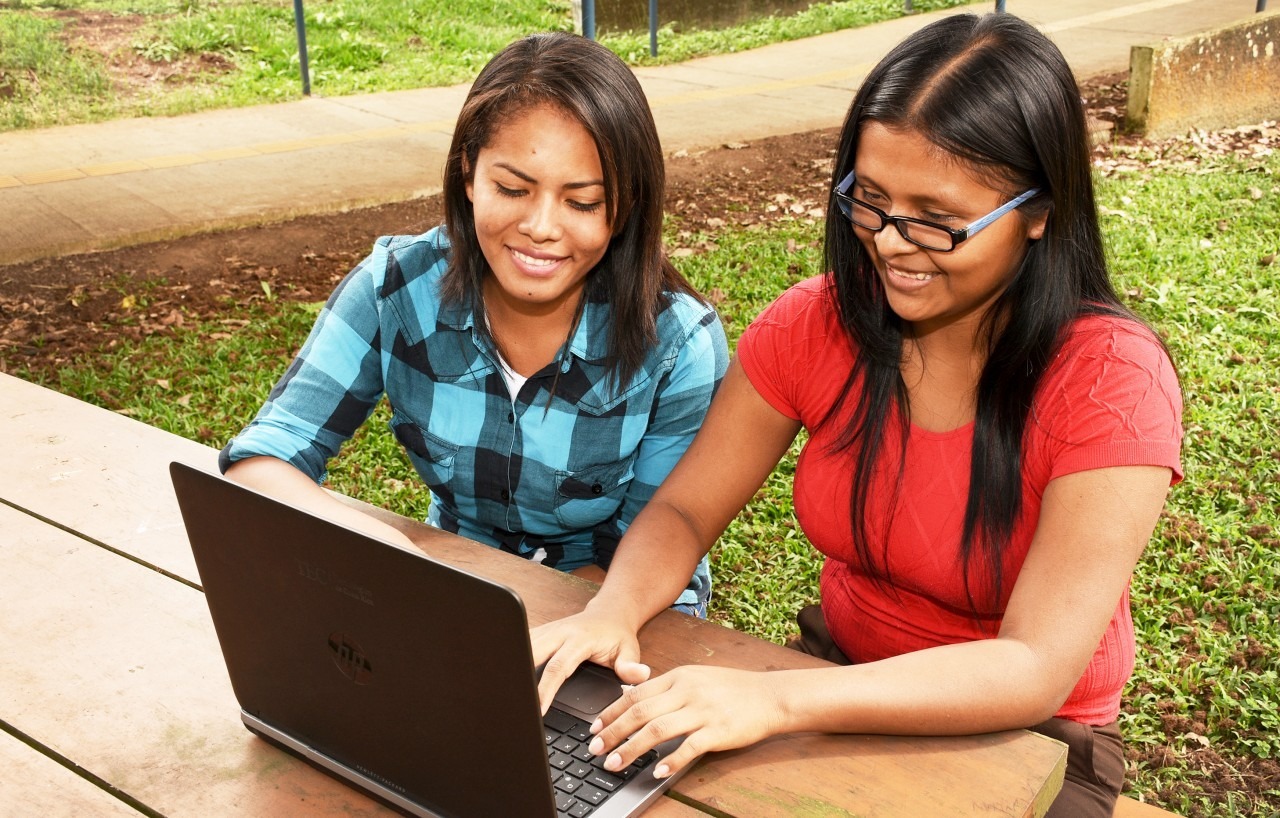 Estudiantes indígenas sentadas utilizando computadora. 