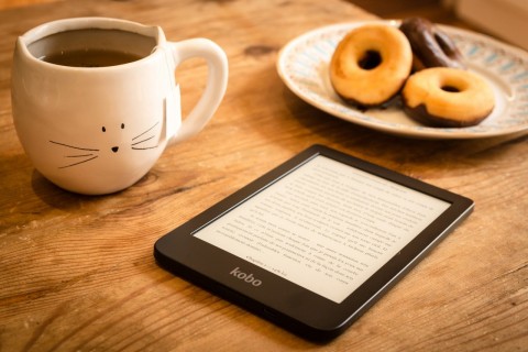 Libro digital acompañado de una taza de café y un plato con galletas.