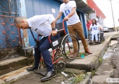 Funcionario municipal cayendo de la silla de ruedas por una acera en mal estado