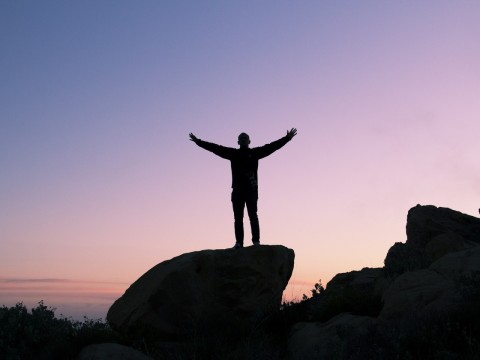 Silueta de una persona en la cima de una montaña levantando los brazos en señal de triunfo.
