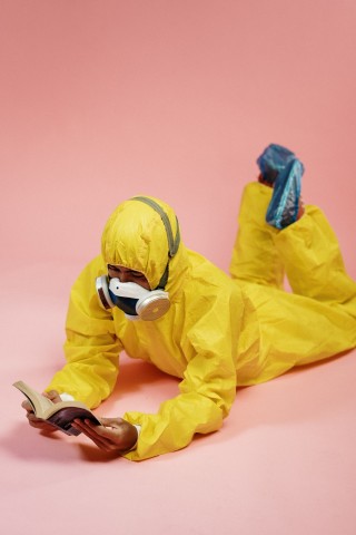 Hombre con traje de protección y mascarilla leyendo un libro acostado boca abajo.