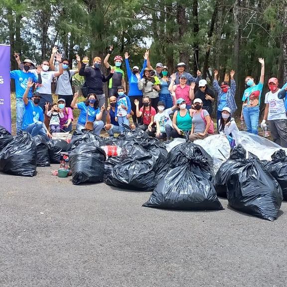 Grupo de 30 personas alzando sus brazos detrás de una gran cantidad de bolsas llenas de residuos sólidos.