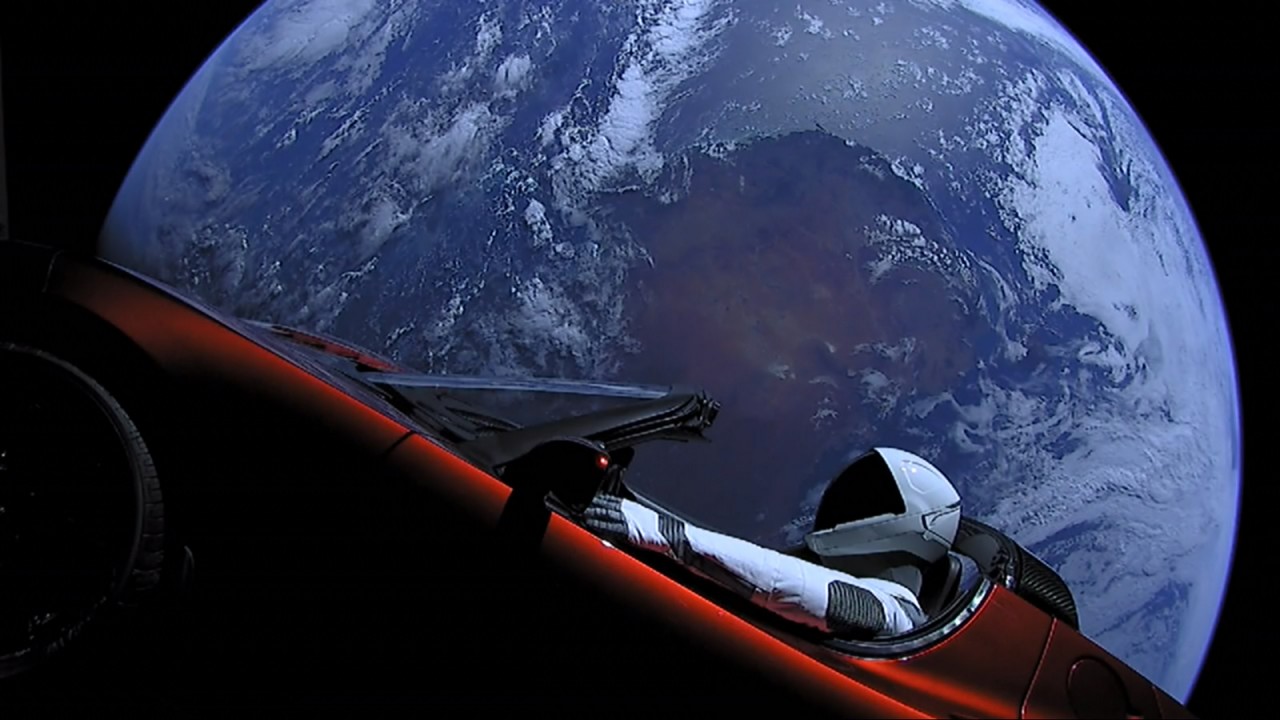 Un auto, con un manequí, en el espacio, frente a la Tierra