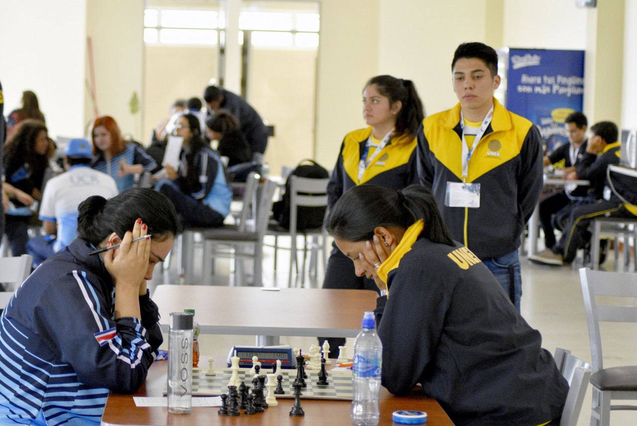 Dos jugadoras de la UNED y la UCR, mientras sus compañeros de equipo observan la partida.400