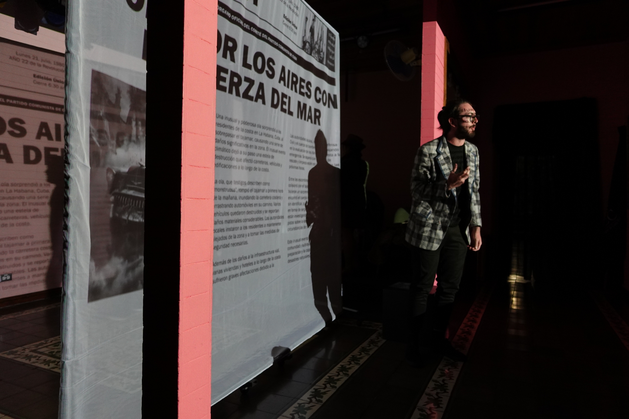 Un hombre se dirige al público frente a la proyección de un diario. 