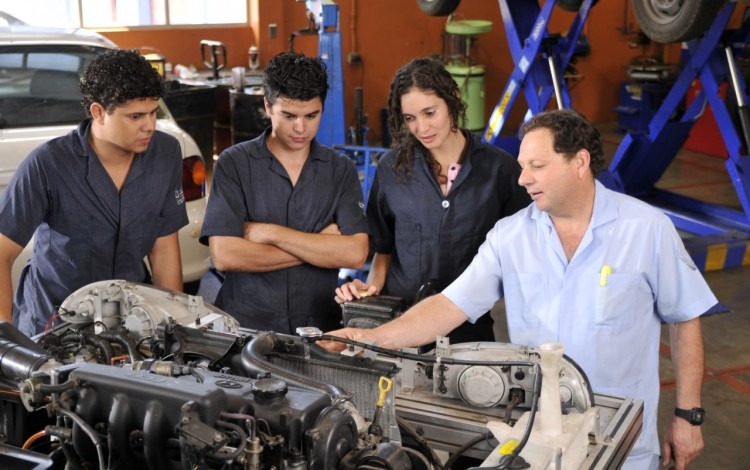 Tres estudiantes observan al profesor explicarles partes de un motor. 