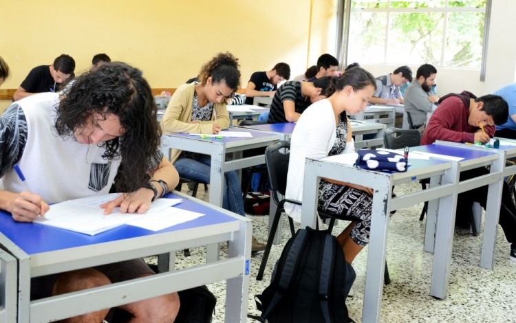 Imagen de varios estudiantes sentados en un pupitre en clases.