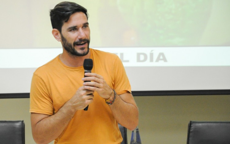 Hombre con un micrófono frente a muchos estudiantes dando una charla.