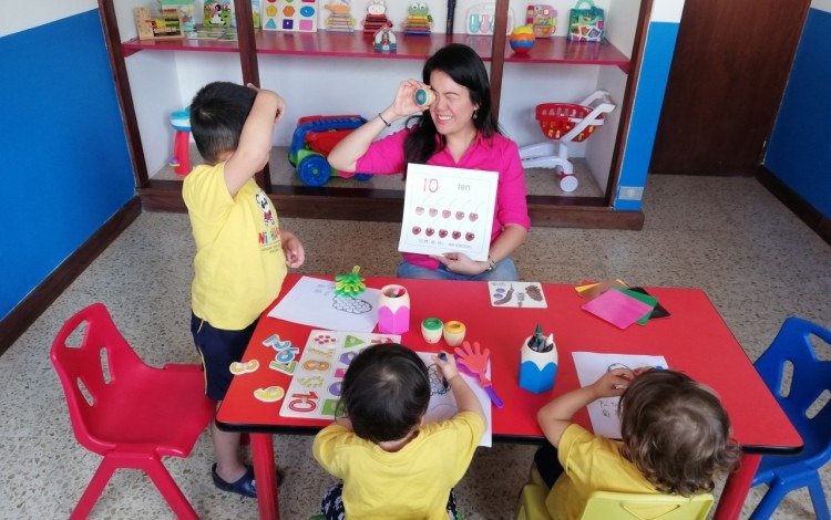 niños en una mesa compartiendo con la maestra en un aula