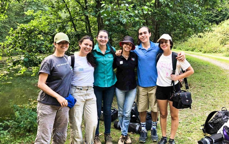 Cinco mujeres y un hombre posan frente a un bosque.