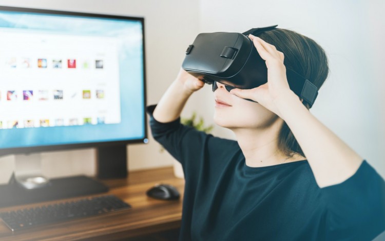 Una joven utilizando un dispositivo de realidad virtual frente al computador.