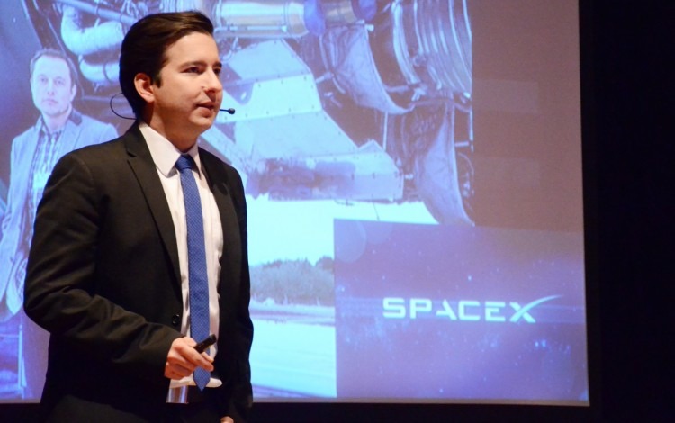 Marco Gómez en el escenario, frente a una proyección que dice SpaceX.