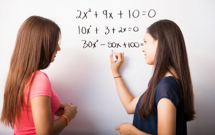 dos mujeres frente a pizarra resolviendo ejercicios de matemática