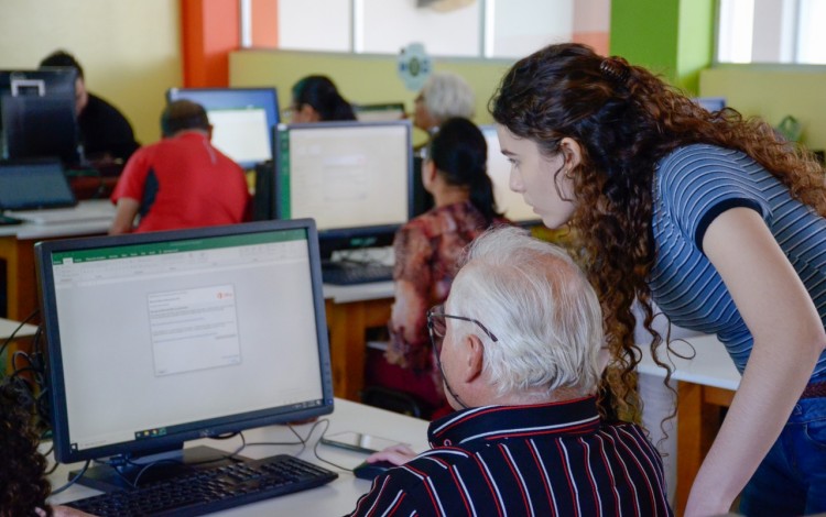 Adulto mayor en computadora asistido por una mujer estudiante.