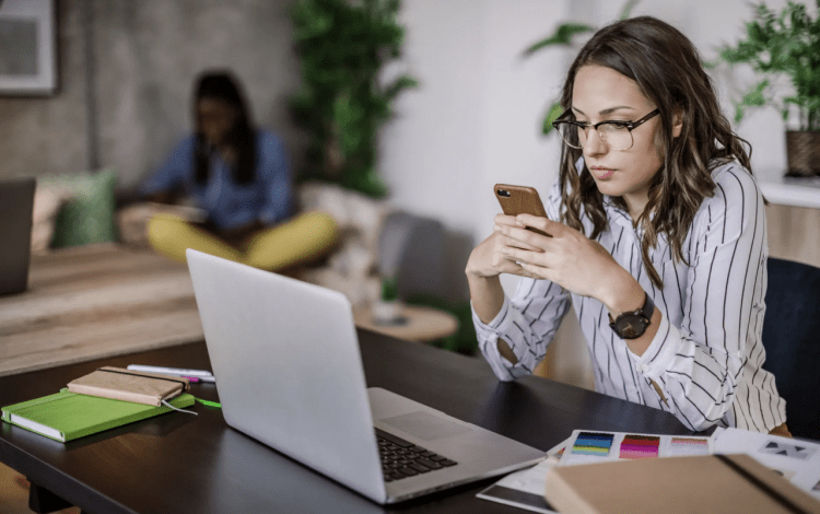 mujer viendo su teléfono frente a computadora