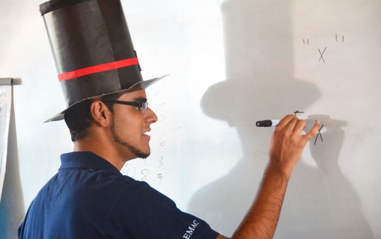 joven con sombrero de mago escribiendo en pizarra signos matemáticos