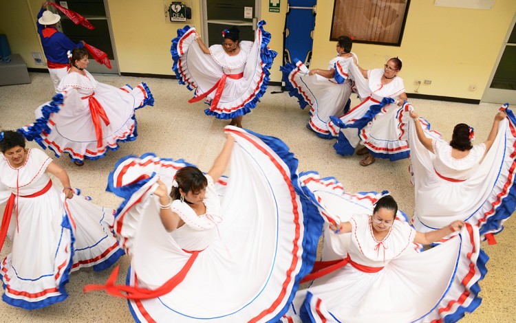 Un grupo de señoras baila con el vestido típico, de color blanco con ribetes azul y rojo.