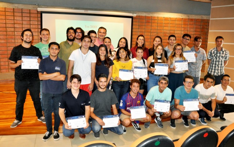 Unos 20 estudiantes muestran sus diplomas, posando junto a los profesores. 