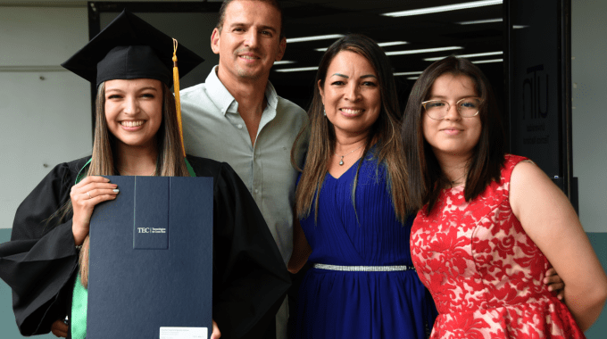 Imagen de la estudiante graduada con el título junto a sus papás y hermana.