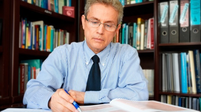 Hombre con corbata y lapicero en mano escribe en libro