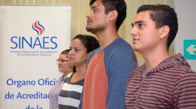 Estudiantes posando a la par de banner con logo de SINAES. 