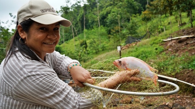 Una mujer sostiene una tilapia que acaba de sacar del agua