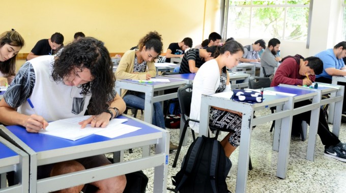 Imagen de varios estudiantes sentados en un pupitre en clases.