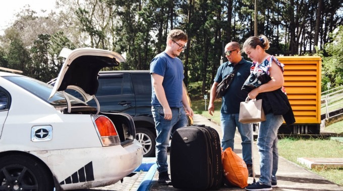 Imagen de un joven  con sus papás  bajando las maletas del carro para vivir en residencias.