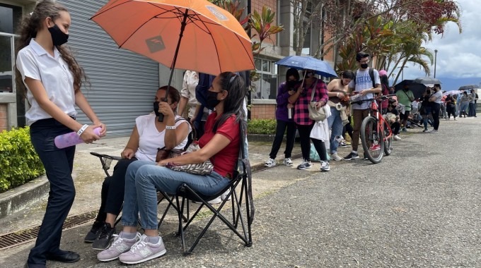 Personas haciendo fila con sombrillas para protegerse del sol.