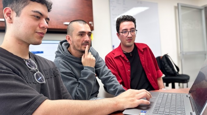 los jóvenes analizan código en la computadora, junto al docente