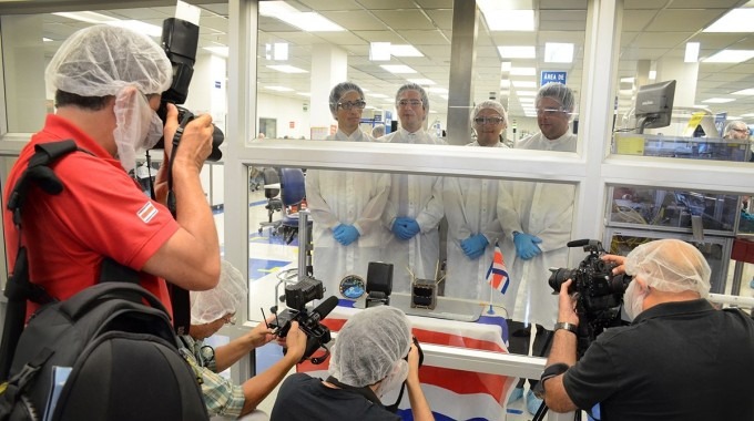 Tres fotógrafos frente a los ingenieros, separados por un vidrio. Los investigadores visten de bata de laboratorio.