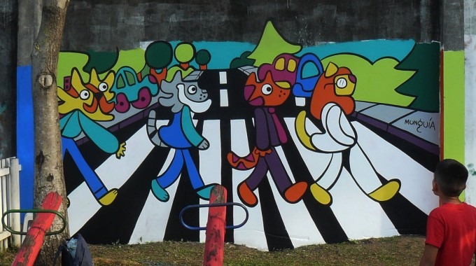 Mural de Munguía en un parque infantil que hace una parodia con gatos de la imagen icónica de la banda The Beatles pasando por un cruce peatonal.