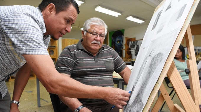 Un adulto mayor aprende a dibujar con la ayuda del profesor.