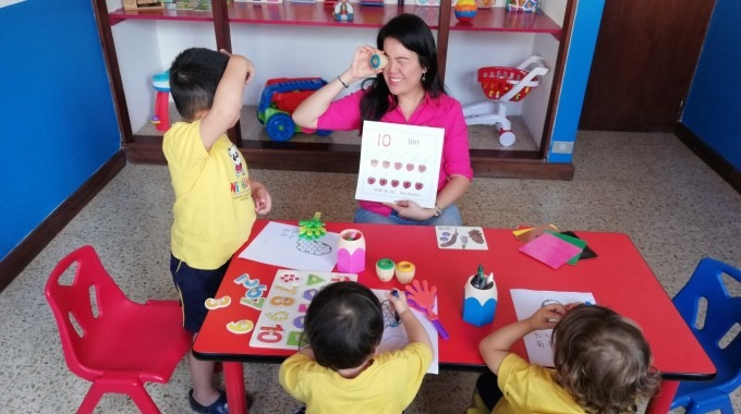 niños en una mesa compartiendo con la maestra en un aula