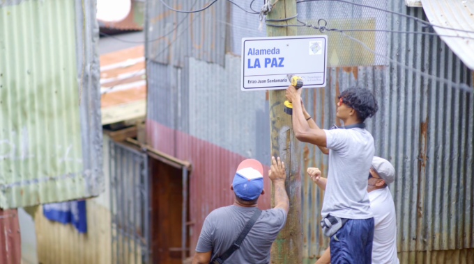 Tres hombres colocan un rótulo en un poste de madera.