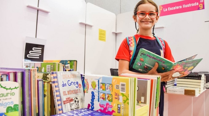 Nina posa junto, en uno de los stands mientras ve un libro 