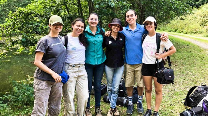 Cinco mujeres y un hombre posan frente a un bosque.