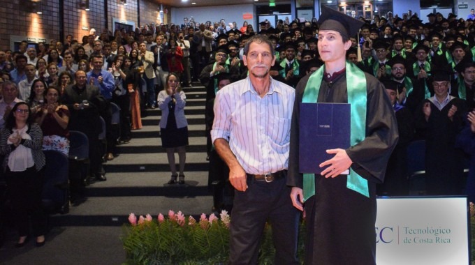 Joven graduado David junto  con su padre y detrás el auditorio con el resto de graduados