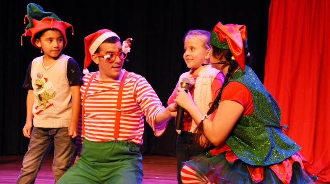 Dos personas sentadas hablando con una niña y un niño, en una obra de teatro.