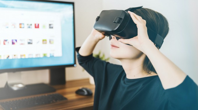 Una joven utilizando un dispositivo de realidad virtual frente al computador.