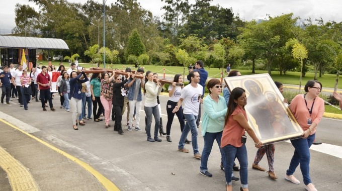 Imagen de funcionarios y estudiantes cargando una cruz y un cuadro con la imagen de la Virgen.