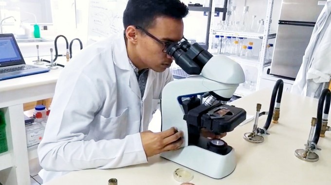 La imagen muestra a José Pablo en el laboratorio viendo a través del microscopio. 