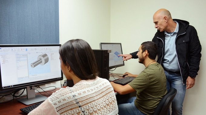 Los estudiantes ven las computadoras mientras el profesor les explica.