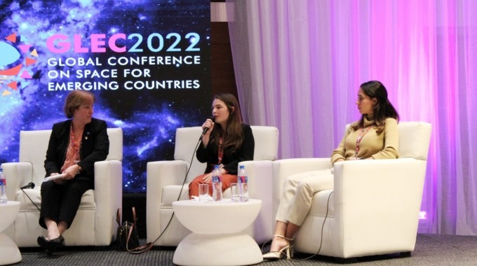 Se observan tres mujeres en el escenario, en un panel de discusión.