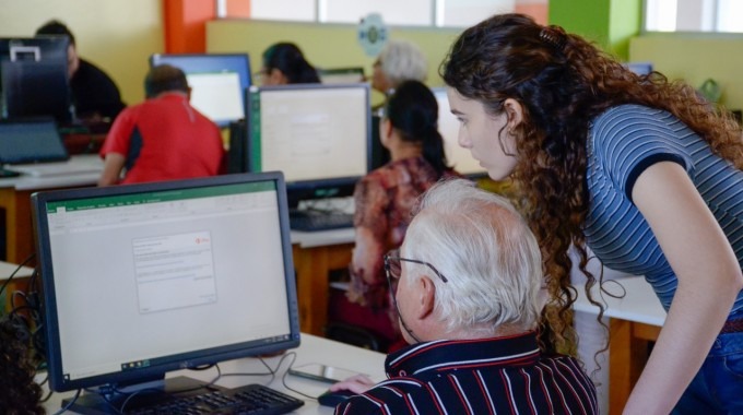 Adulto mayor en computadora asistido por una mujer estudiante.
