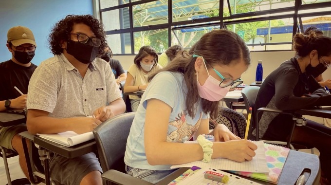 jóvenes en una clase en el TEC. La principal es una muchacha tomando notas. 