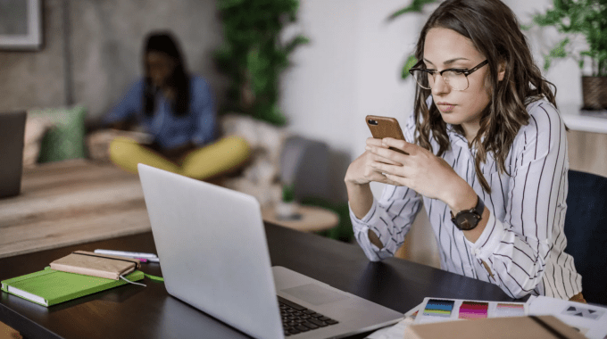 mujer viendo su teléfono frente a computadora