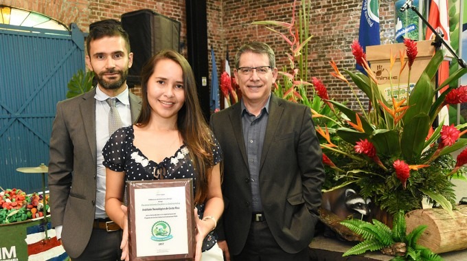 La regente ambiental sostiene el premio, acompañada del rector y el coordinador de la unidad de gestión ambiental.