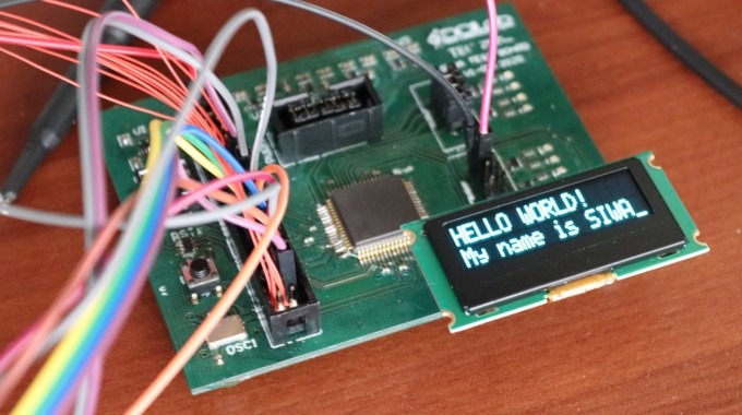 Tarjeta de circuitos, con cables y una pantalla que dice Hello World, My name is SIWA