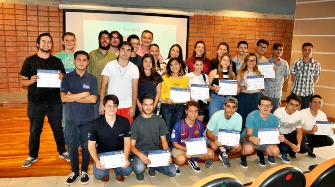 Unos 20 estudiantes muestran sus diplomas, posando junto a los profesores. 